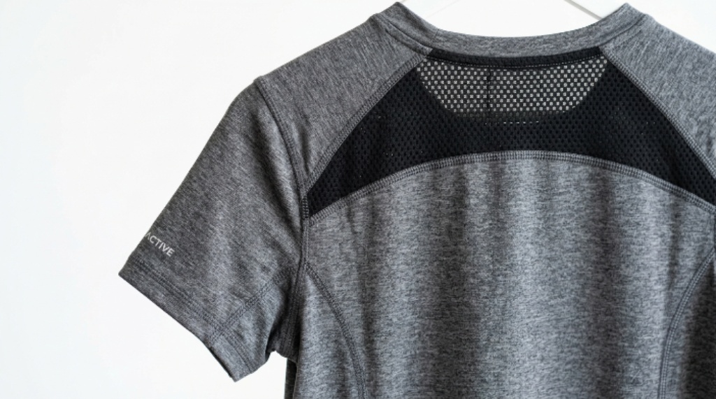 Close-up of a women's breathable gym tee with mesh panel detail and flatlock seams on a white background