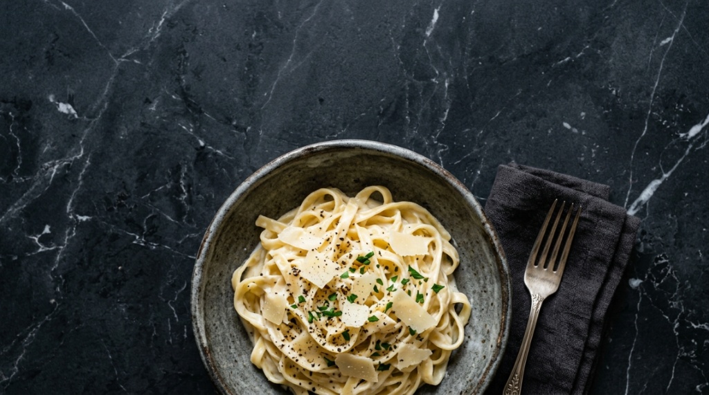 Creamy fettuccine pasta in a rustic bowl on a dark marble table.